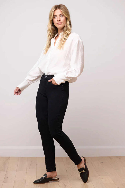 A woman wearing the RACHEL Woven Classic Rise Skinny Yoga Jeans in Pitch Black, stnding in front of a white wall 
