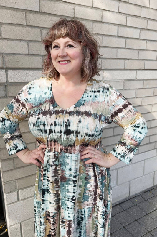 A 3/4 shot of a woman wearing the Denver Dress by Pure Essence in Multicolour Print, with a V-neck, long sleeves, gathered waist, and long tiered skirt 