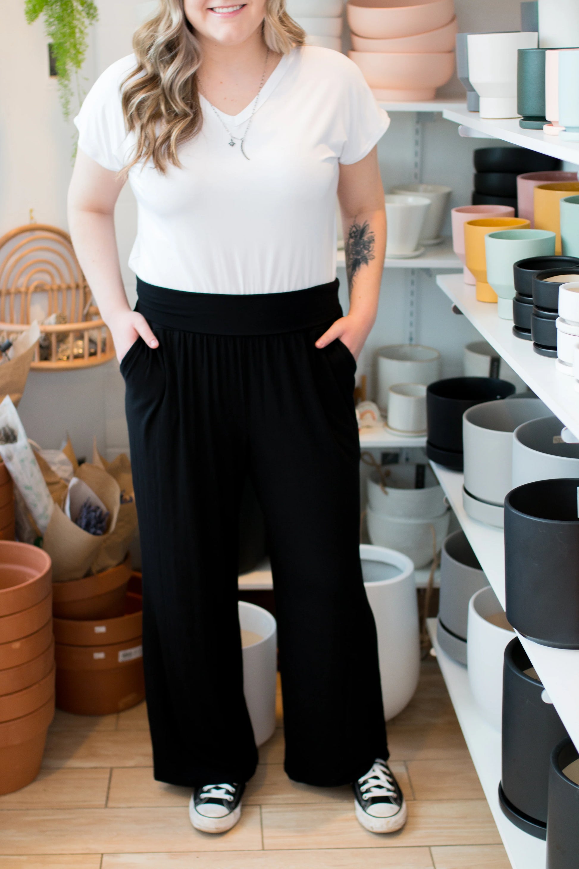 A woman wearing the Bree Wide Leg Pants by Ang Hill in Black, cropped wide-legged pants with a high elastic waist band and deep pockets. She is wearing them with a white t-shirt and standing in a pottery studio. 