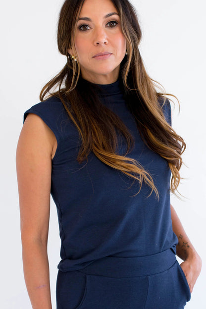 Woman wearing the Dori Mockneck navy sleeveless top from Ang Hill, standing against a white background