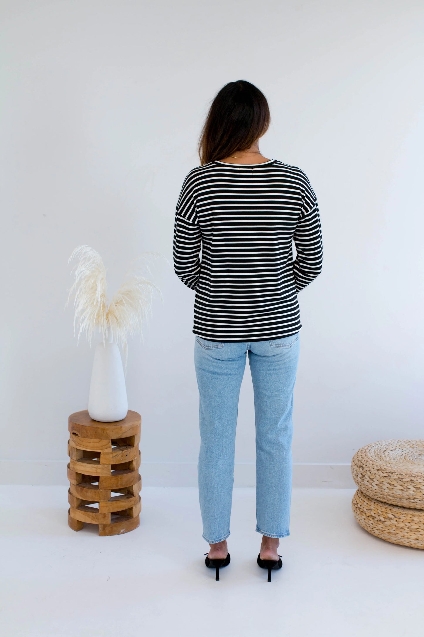 Back view of a woman wearing the Munro Bamboo Crewneck sweater by Ang Hill in black and white stripes. She is wearing it with light blue jeans against a white background.