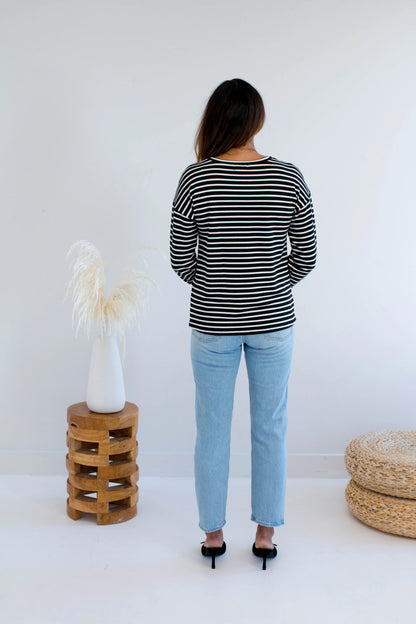 Back view of a woman wearing the Munro Bamboo Crewneck sweater by Ang Hill in black and white stripes. She is wearing it with light blue jeans against a white background.