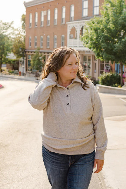 A woman wearing the Classic Coastal Sweater by Blondie in Flax, a relaxed fit sweatshirt with a collar and four button placket. She is wearing it with jeans and standing in the street. 