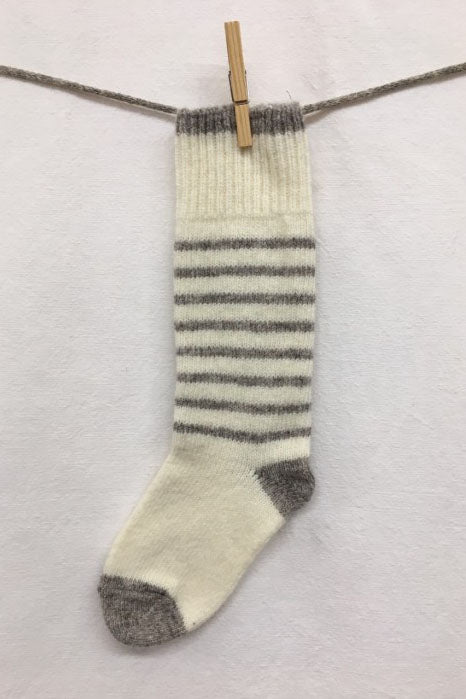 Knitted Socks by Charlevoix Pure Laine in Natural/Grey stripe are shown hanging on a clothesline against a white background