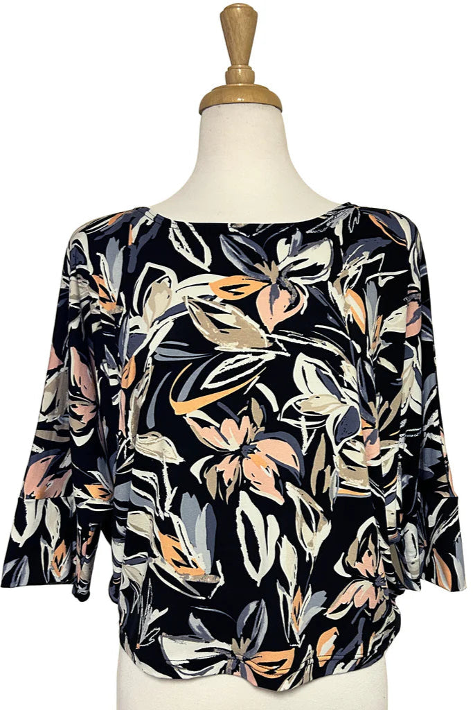 The Batwing Top by Desserts and Skirts in Blush/Black floral print, a loose top with a boat neck and flowing 3/4 sleeves, is shown on a mannequin in front of a white background. 
