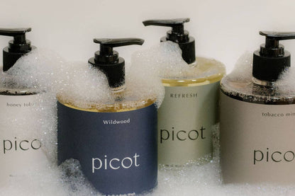 Four Picot soap dispensers in different colours with visible branding in a bubble bath.
