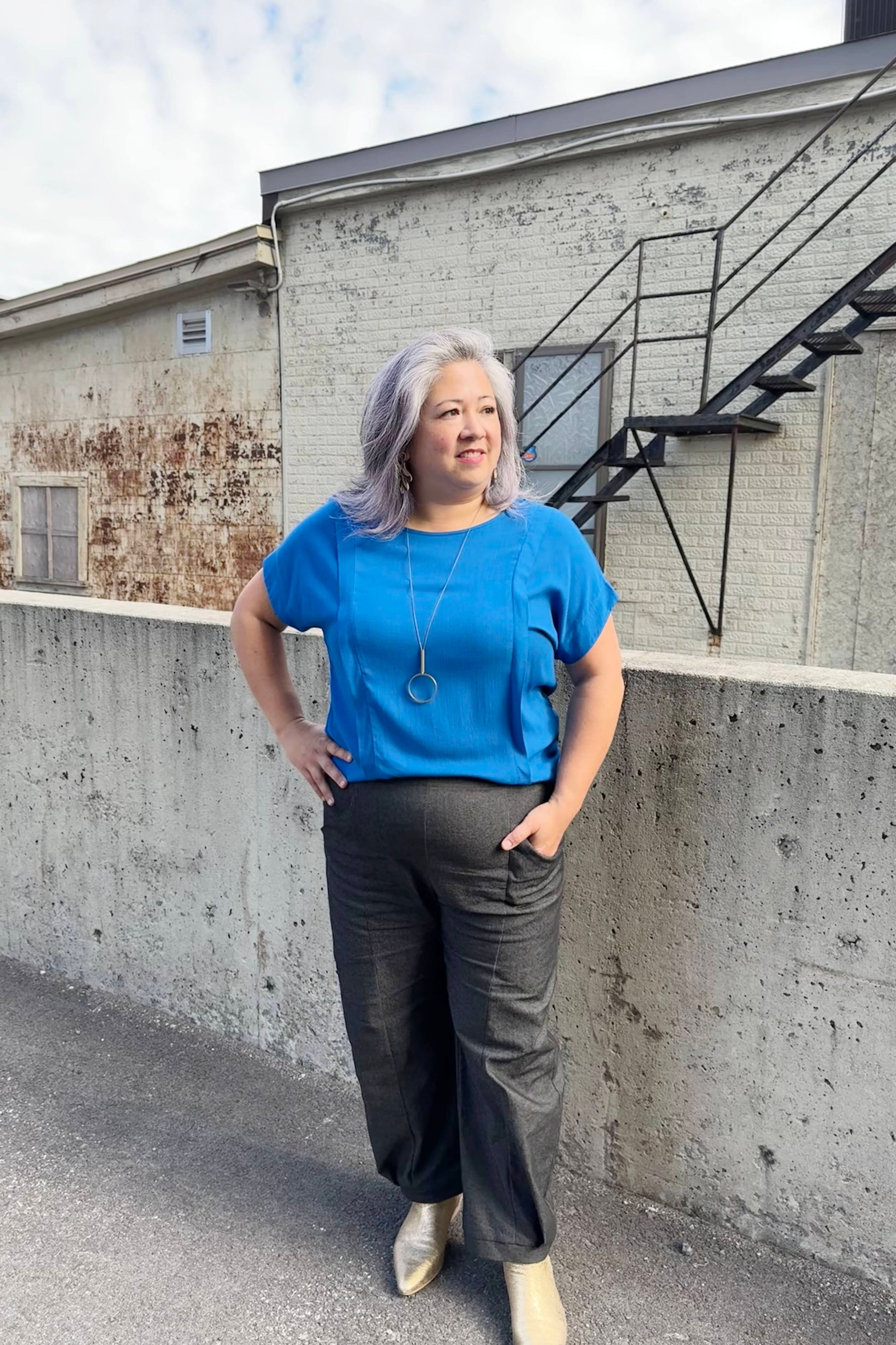 A woman A woman wearing the Fuzzy Top by Cokluch in Colbalt with the Thela Pants by Kazak in Black Denim, standing outside in front of a brick building