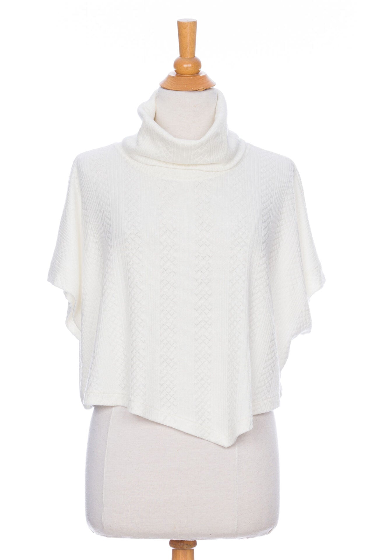 The Lupin Poncho-Bolero in Ivory by Rien ne se Perd, featuring soft jacquard knit, a loose turtleneck, and an asymmetrical hem, is shown on a mannequin in front of a white background. 