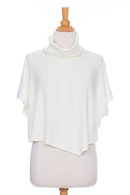 The Lupin Poncho-Bolero in Ivory by Rien ne se Perd, featuring soft jacquard knit, a loose turtleneck, and an asymmetrical hem, is shown on a mannequin in front of a white background. 
