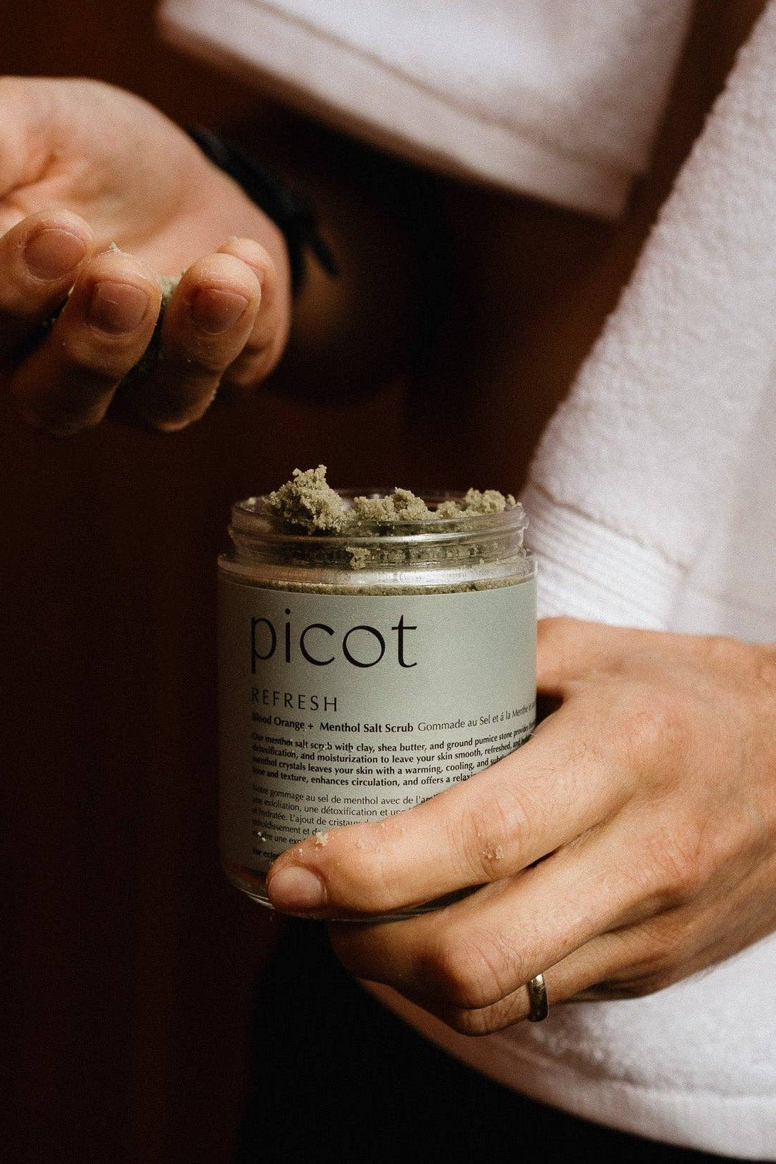 Person holding a jar of Picot salt scrub with a towel draped over their shoulder.