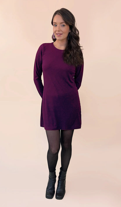 Woman wearing a the Nebulous Dress by Canopée in Pink, a mid-thigh length dress with long sleeves in rib knit. She is standing in front of a  beige background. 