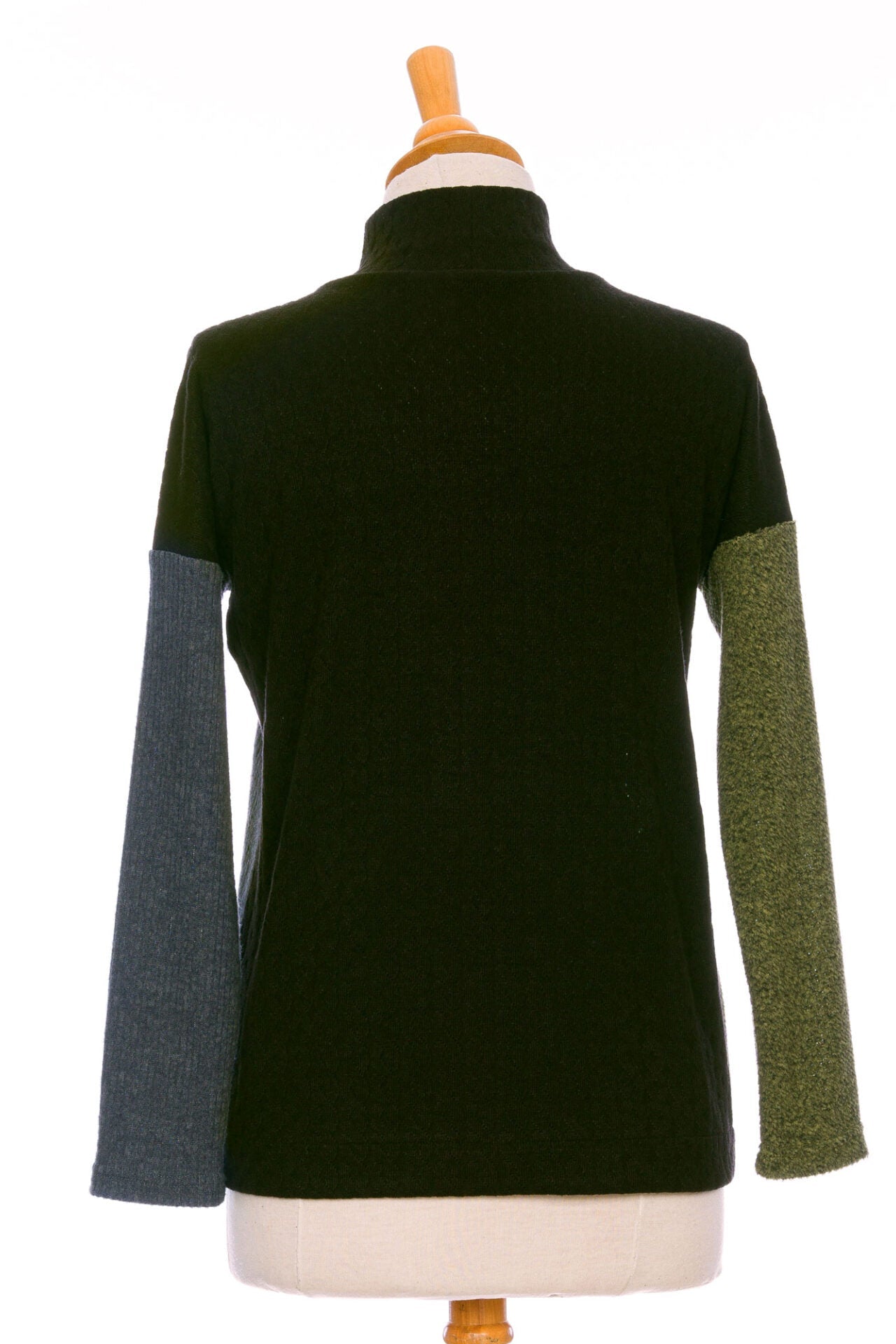 A back view of the Chèvrefeuille Sweater by Rien ne se Perd in Sage, a multi-toned piece that's green on the right side, grey on the left, with a black back, is shown on a mannequin in front of a white background.  It has a cross-over front with five black buttons. 
