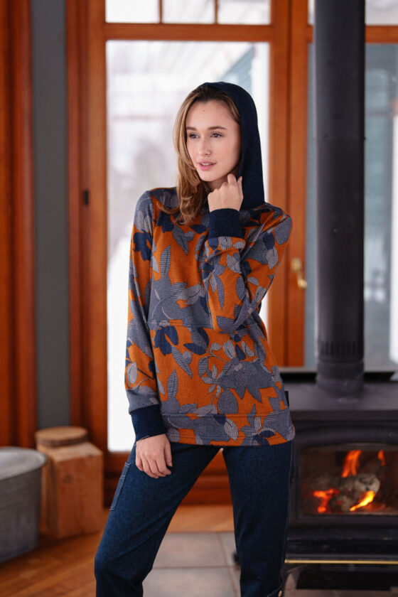 A woman wearing the Lautrec Sweater by Rien ne se Perd in Navy Foliage with jeans stands in front of a wood stove. 