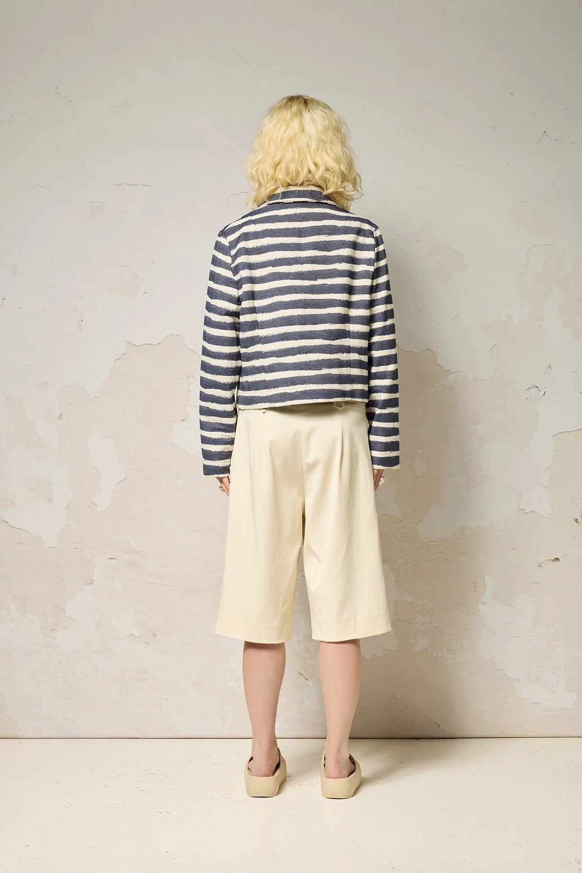 Back view of a woman wearing the Vesta Jacket by Cokluch in Denim Stripe over a denim top and beige pants against a plain background