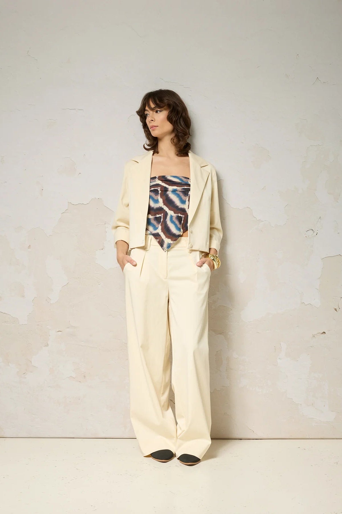 A woman wearing the Vesta Jacket by Cokluch in Vanilla over a patterned top and matching pants against a plain background