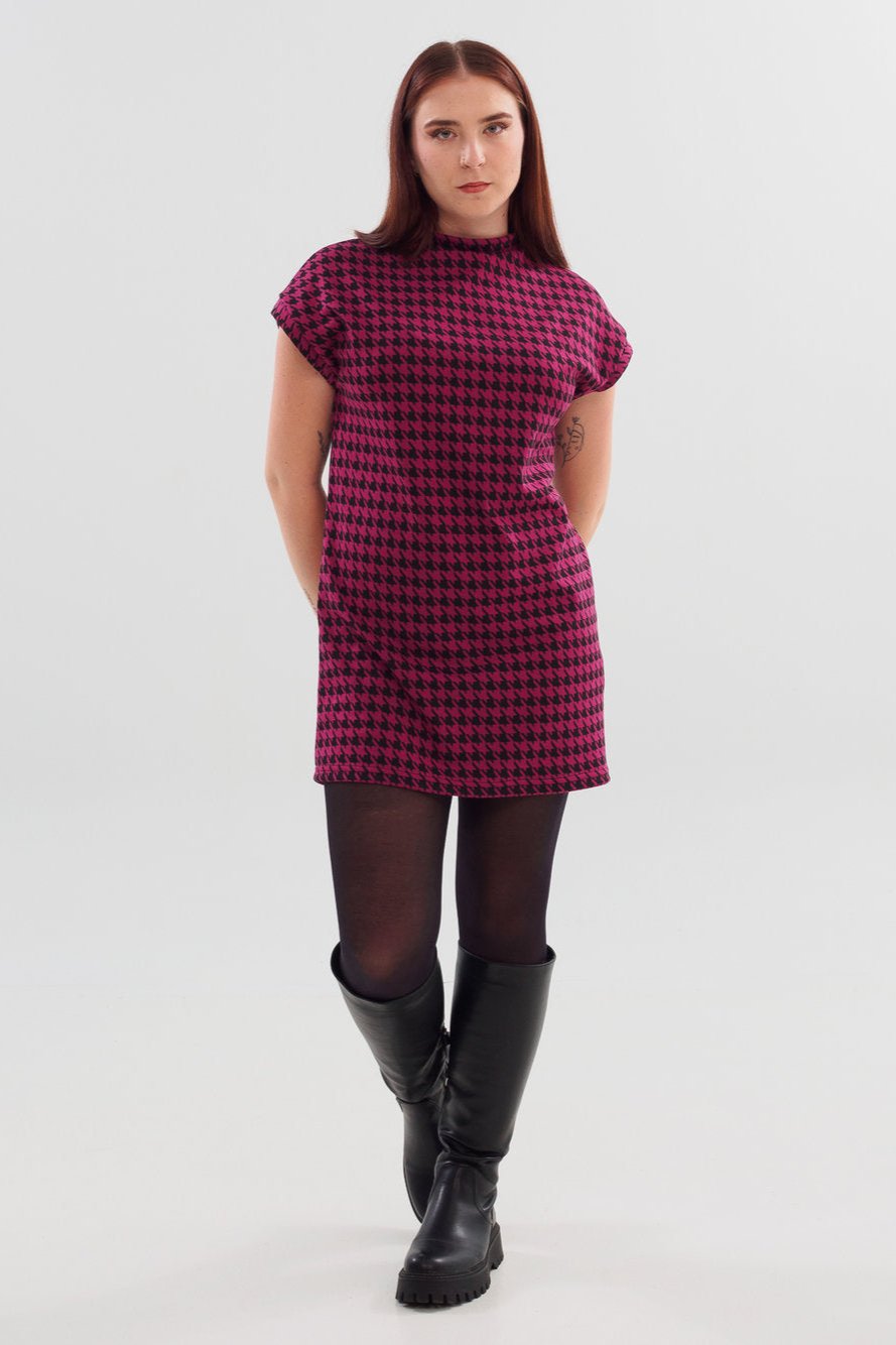 A woman wearing the Cyndi Tunic by Slak in Black and Fuschia houndstooth with black leggings, standing in front of a white background 