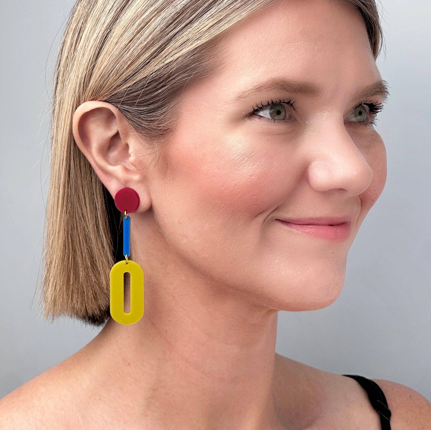 Woman wearing colorful earrings against a neutral background