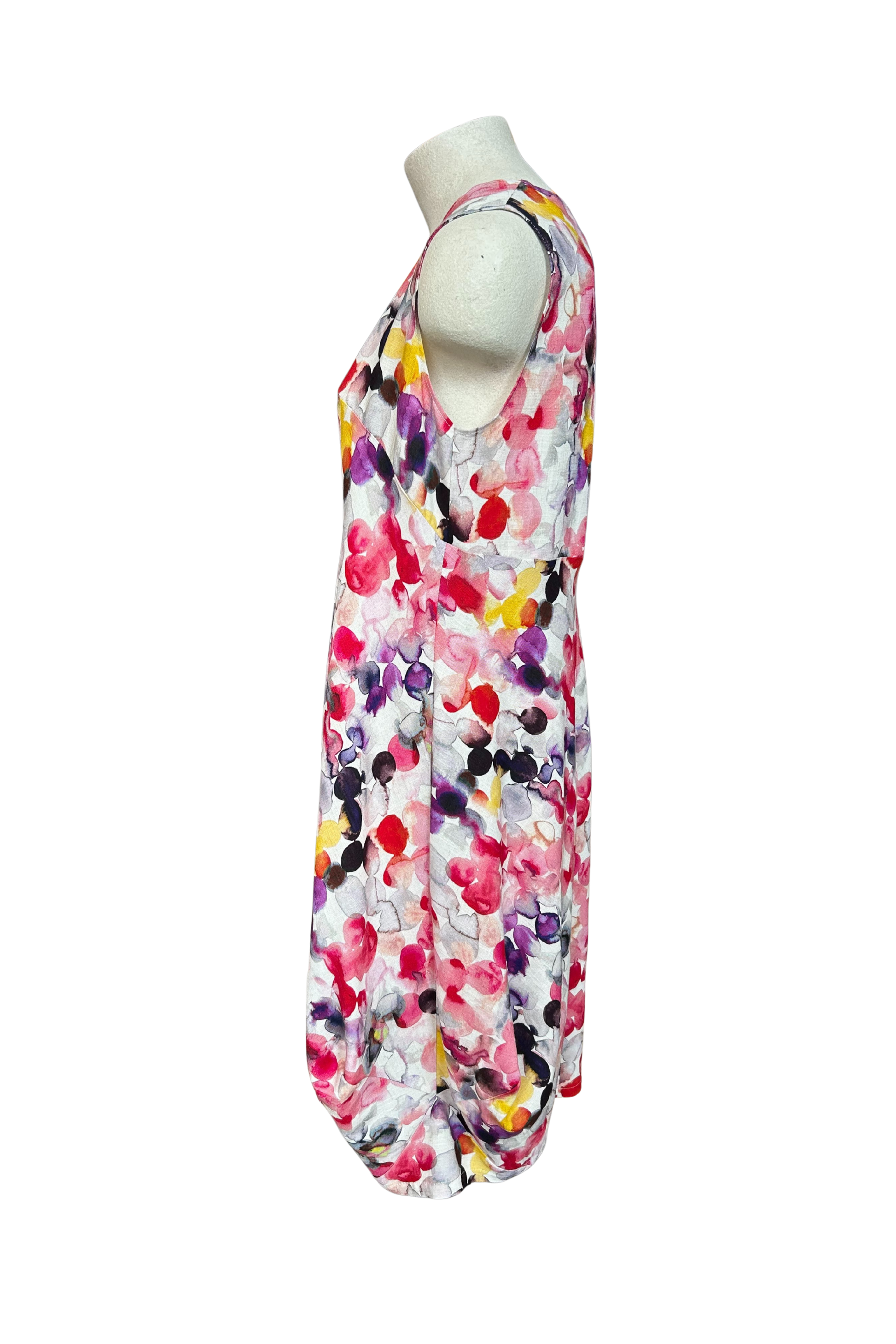 A side view of the Monica Dress by Solomia in Watercolour Print is shown on a mannequin against a white background. It's a sleeveless knee-length dress with a relaxed fit and uniquely angled bottom hem. 