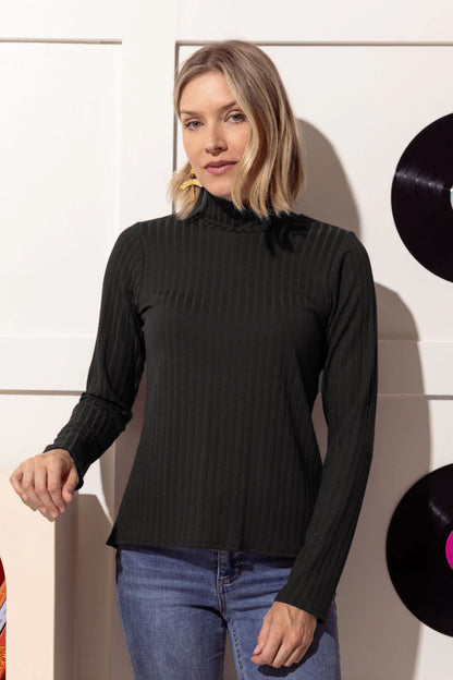 A woman wearing the Elton Sweater by Cherry Bobin with jeans, standing in front of a white wall 