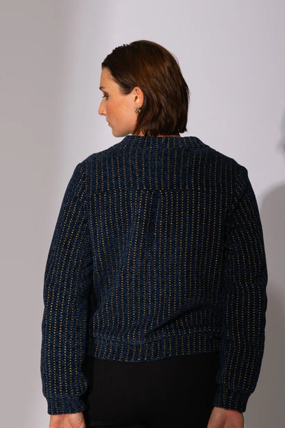 Back view of a woman wearing the Gold Lion Knit Cardigan by Eve Lavoie in Navy, featuring a V-neck, gold thread embedded in the navy fabric, gold buttons, and bias pockets. 