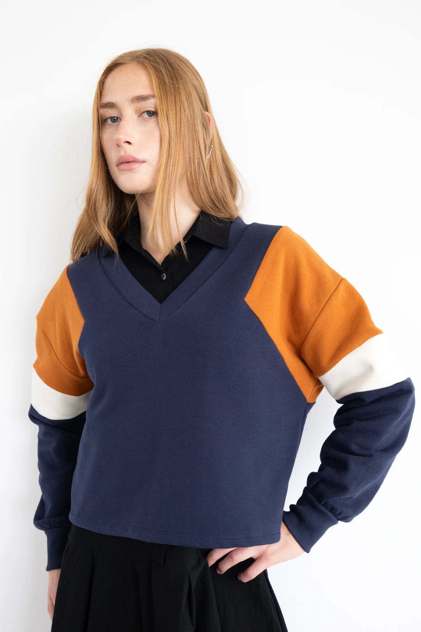A woman wearing the Sinclair Sweatshirt by Eve Lavoie in Navy, a relaxed sweatshirt with a V-neck and colour-blocked panels. She's wearing it with black pants and standing against a white background.