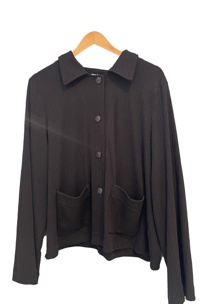 The Fern Jacket by Pure Essence in Black, a boxy jacket with a lapel collar, button front and patch pockets in a ribbed fabric, is shown hanging in front of a white background. 