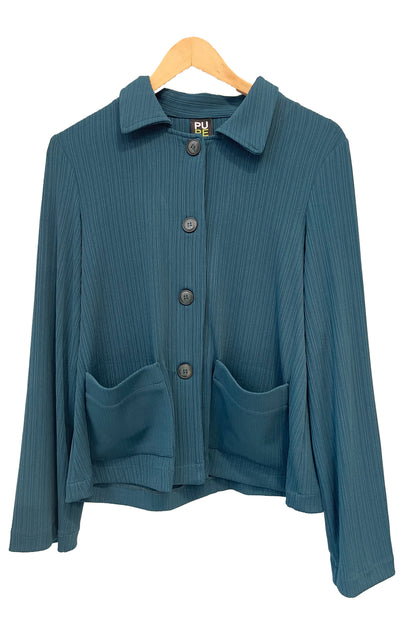 The Fern Jacket by Pure Essence in Spruce, a boxy jacket with a lapel collar, button front and patch pockets in a ribbed fabric, is shown hanging in front of a white background. 