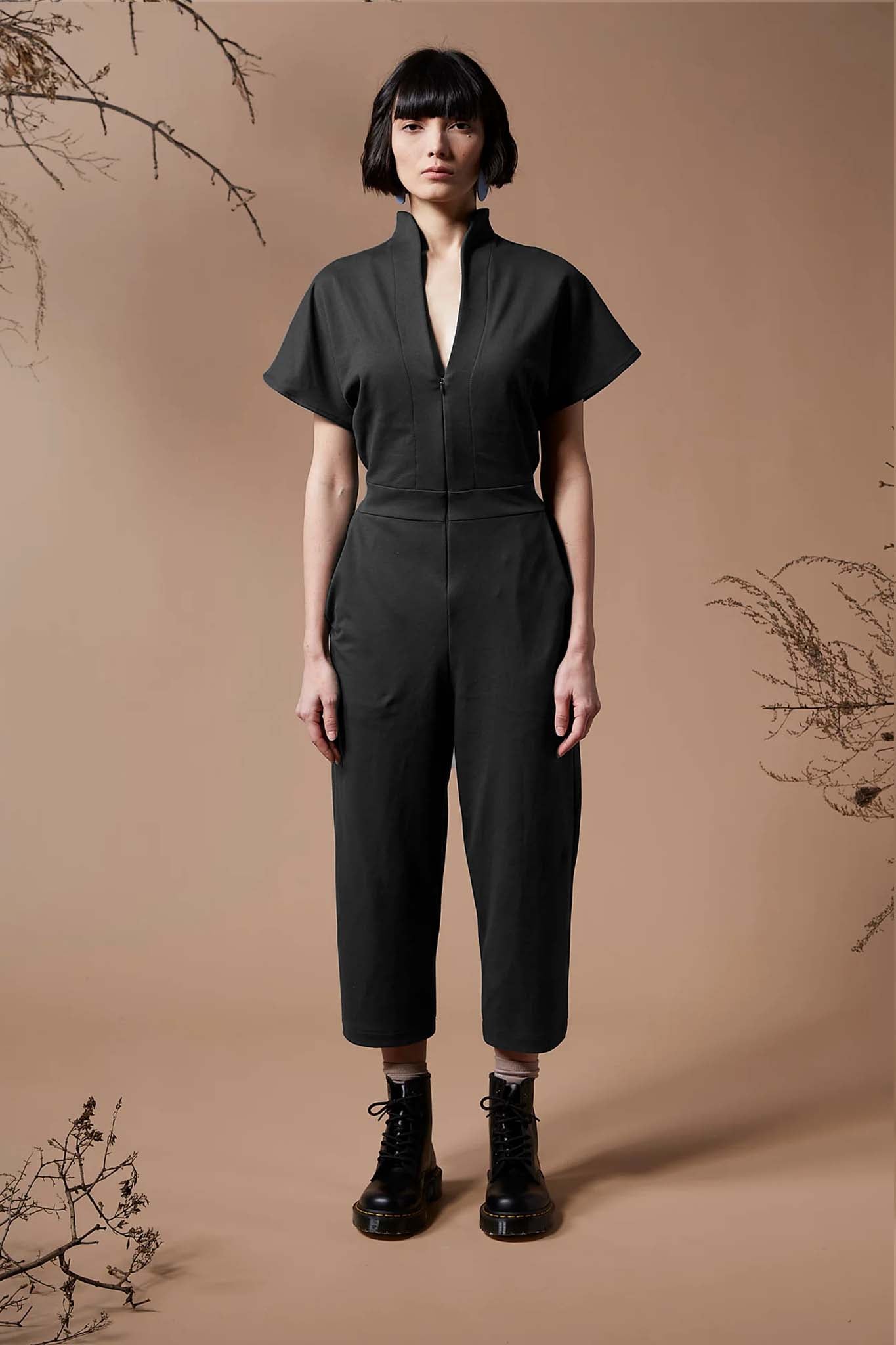 A woman wearing the Jayden Jumpsuit by Melow in Black, standing in front of a beige background