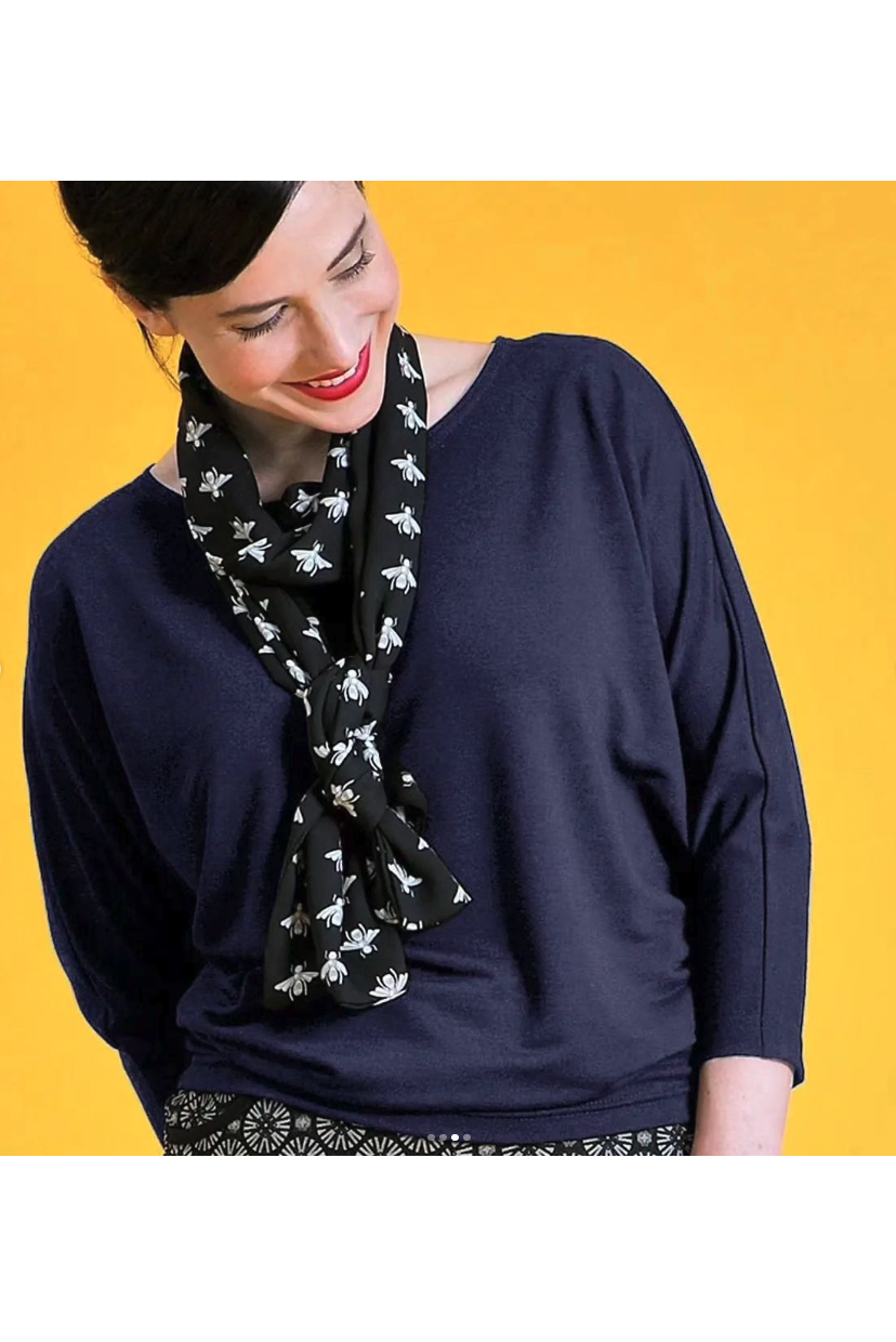 Waist-up view of a woman wearing the Jo Slouch Tee by Mandala in Cadet with a scarf, standing in front of a yellow background 