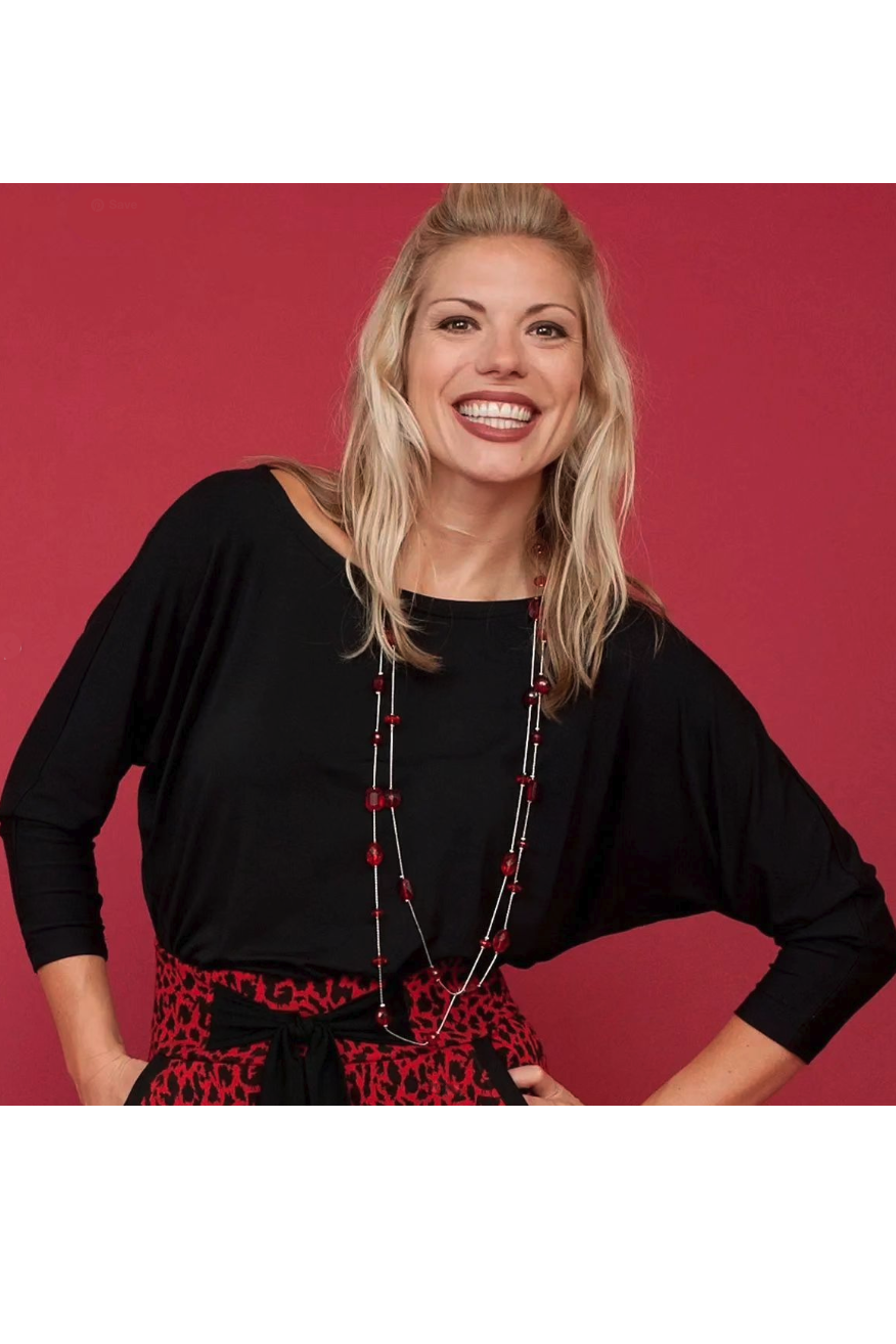 Waist up view of a woman wearing the Jo Slouch Tee by Mandala in Black, standing  in front of a red background 