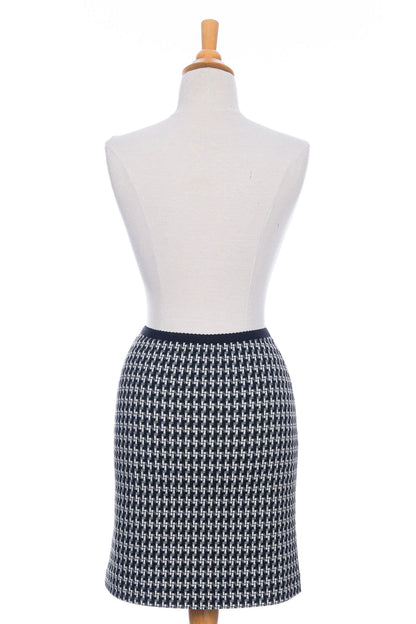 A back view of the Meleze Skirt by Rien ne se Perd in Black and White houndstooth, a knee-length straight skirt with an elastic waist, is shown on a mannequin in front of a white background. 
