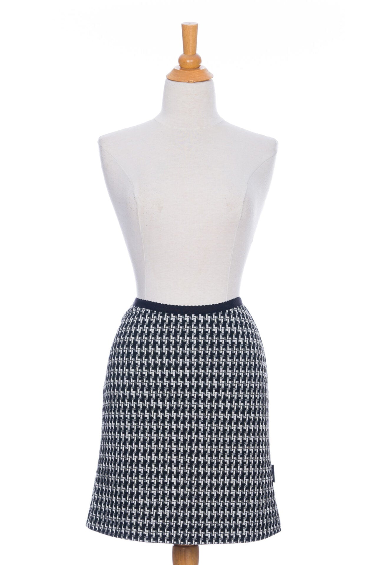The Meleze Skirt by Rien ne se Perd in Black and White houndstooth, a knee-length straight skirt with an elastic waist, is shown on a mannequin in front of a white background. 
