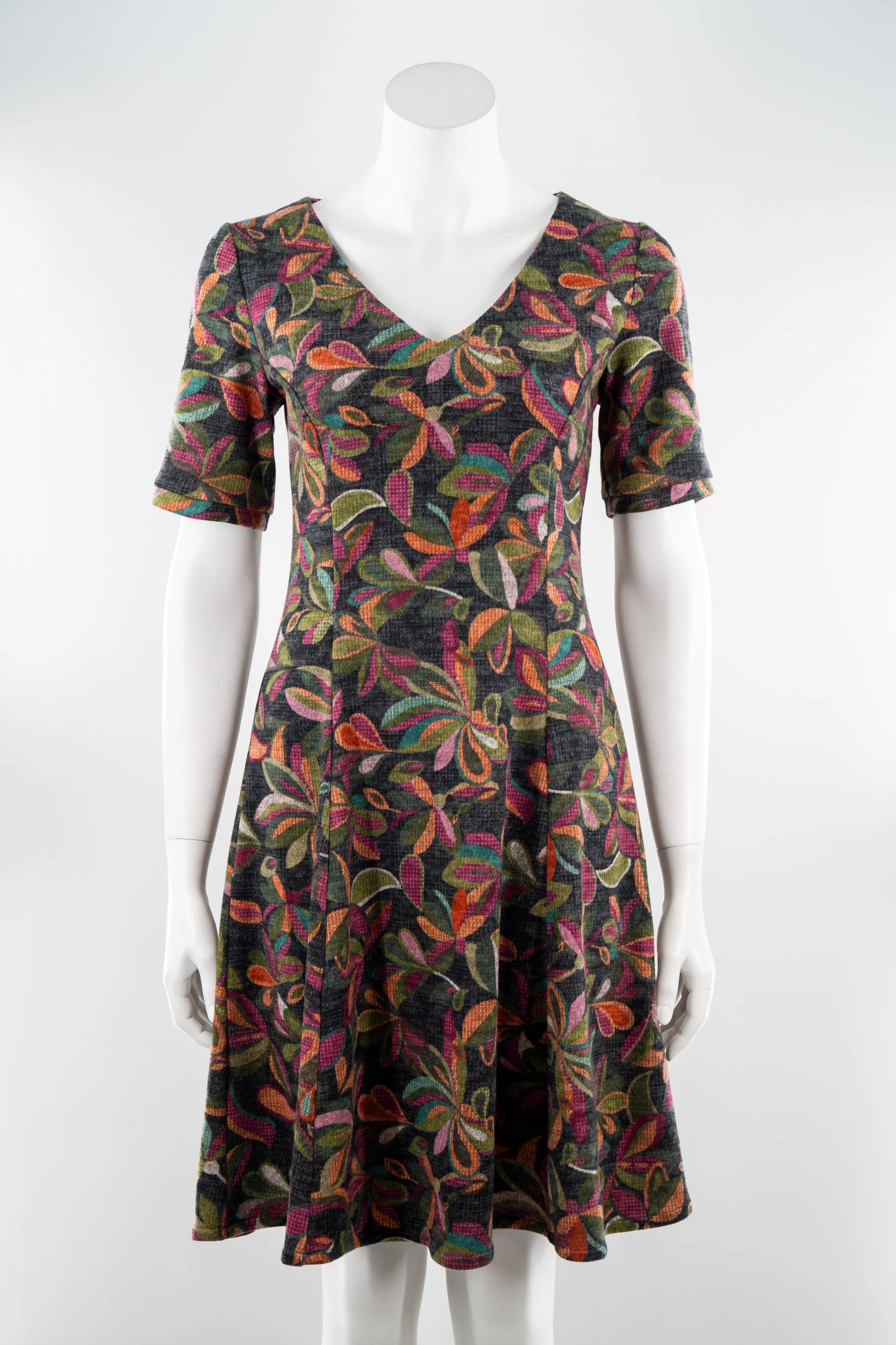 The Botanical Dress by Karkass in Floral, a knit dress with a V-neck, elbow length sleeves, fit and flare shape, and above the knee hem, is shown on a mannequin in front of a white background. 