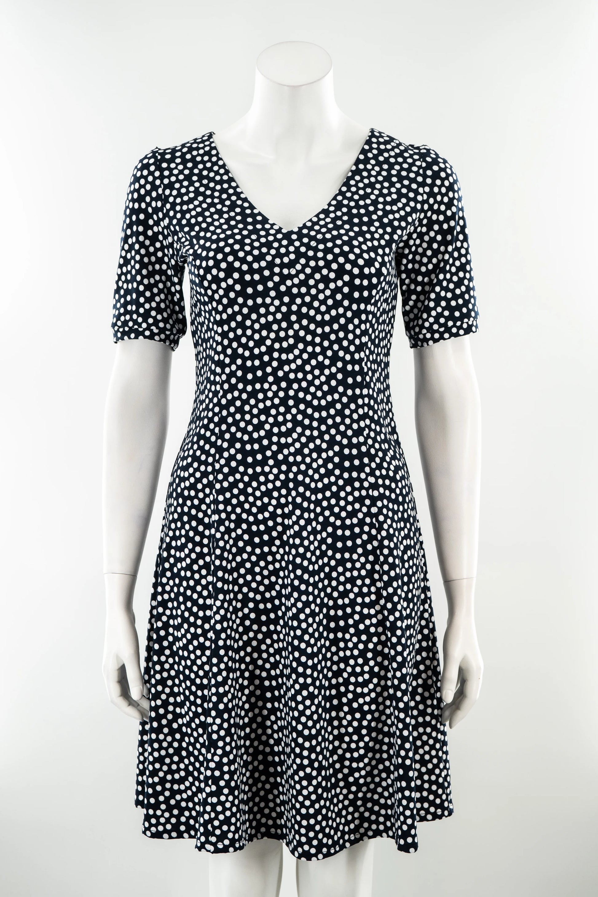 The Navy Polka Dot Dresss by Karkass is shown on against a white background. It has a v-neck, short sleeves, princess seams, and an above the knee hem. 