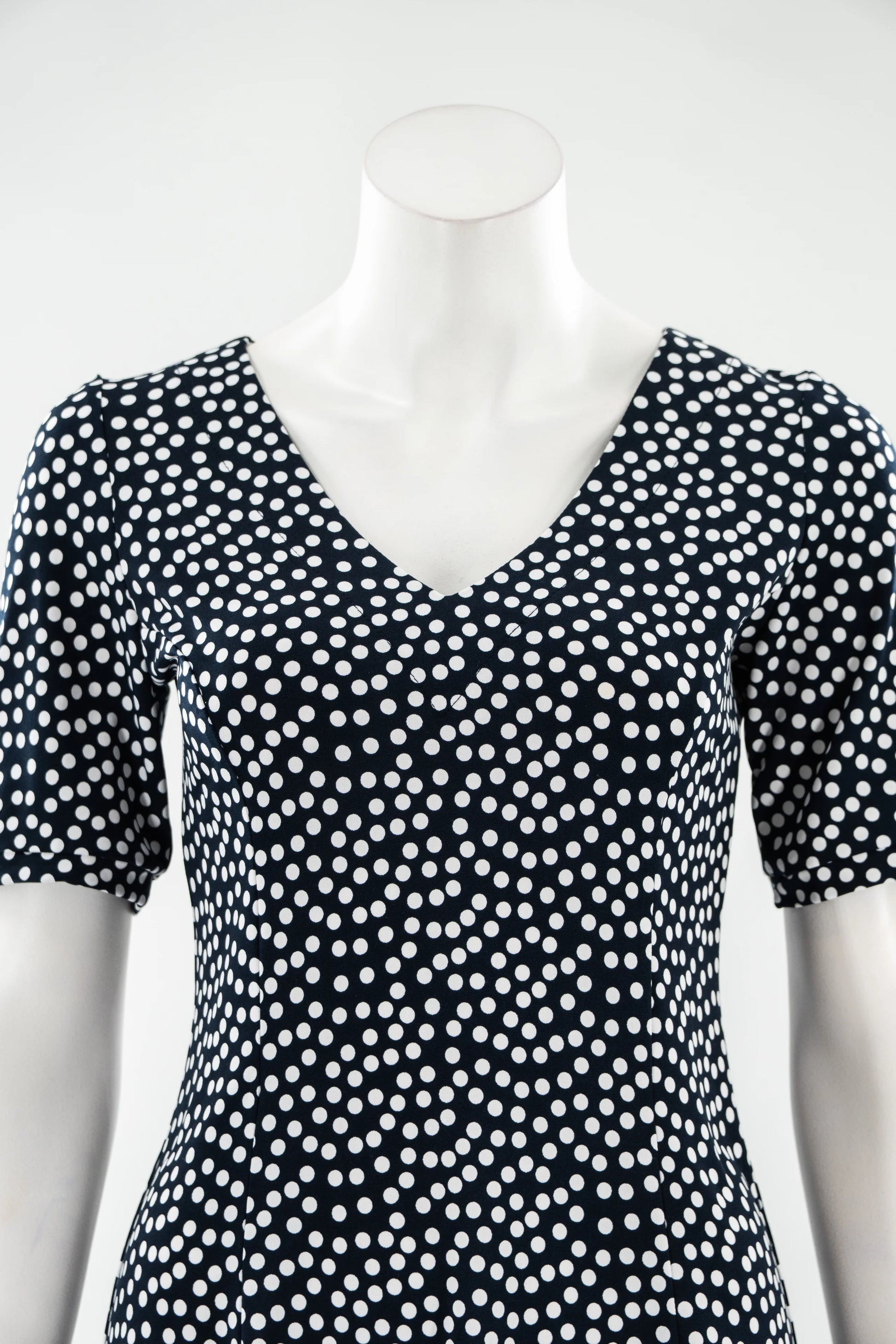 The Navy Polka Dot Dresss by Karkass is shown on against a white background. It has a v-neck, short sleeves, princess seams, and an above the knee hem. 