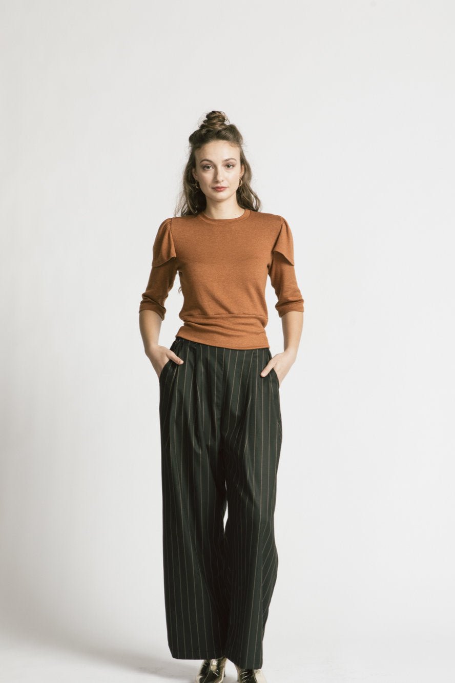 A woman wearing the Katherine Pants by Allison Wonderland in Pinstripe, with the Eyre Sweater in Caramel, standing in front of a white background 