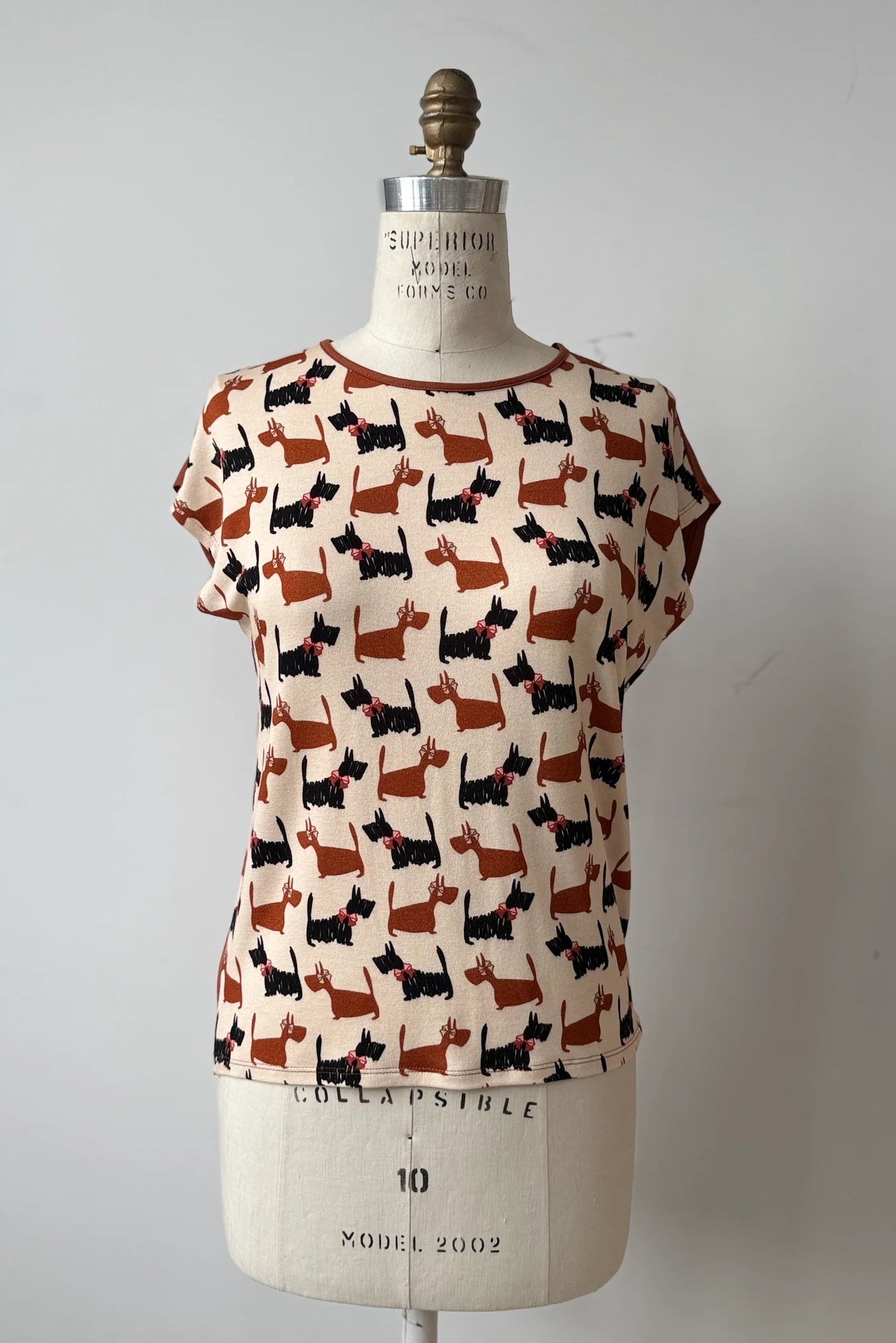 The Arty T-Shirt by Kollontai in Dogs/Rust print, with a round neck, short extended sleeves, and a slight hi-low hemline, and a solid rust back, is shown on a mannequin against a grey background. 
