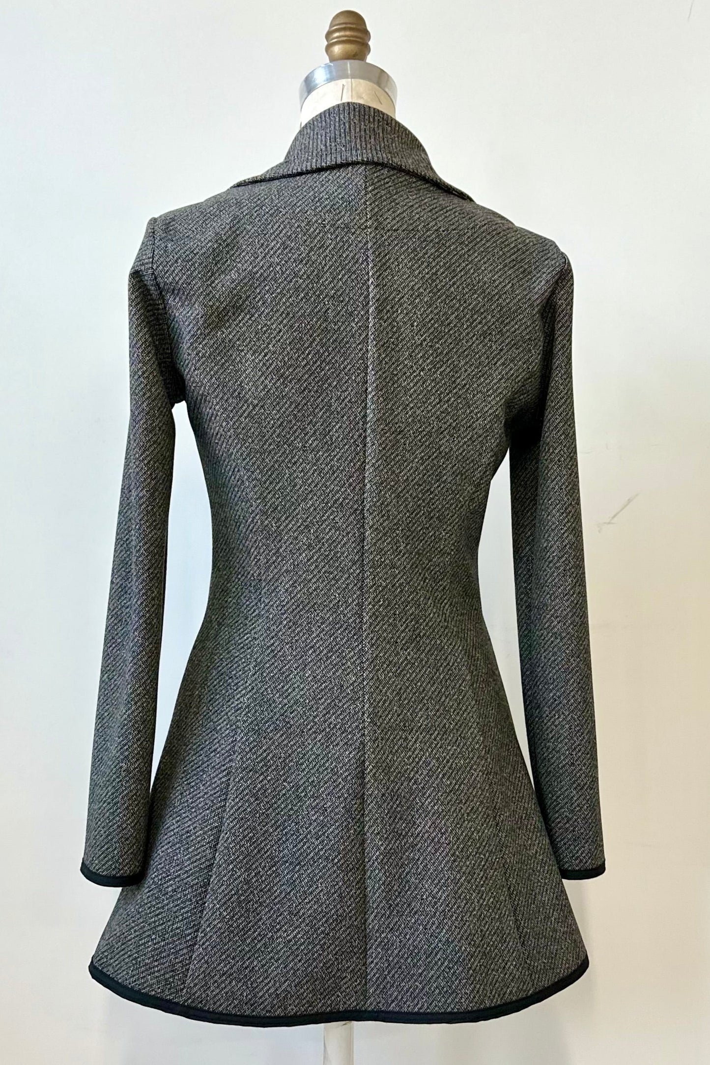 Back view of the Henderson Jacket by Kollontai in Charcoal tweed, with a fitted A-line shape that flares from the waist, a classic collar, and buttons down the front, shown on a mannequin in front of a white background. 