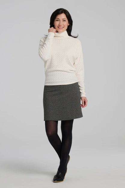 A woman wearing the Frost Skirt by Kollontai in Charcoal tweed, an above the knee length A-line skirt with an elastic waist.  She is wearing it with the Plume Top in and standing in front of a grey background. 