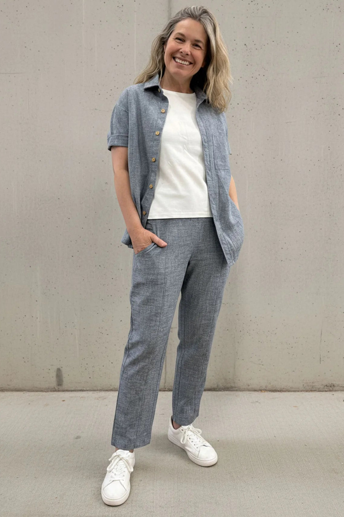 A woman wearing the Cantley Short Pants by Message Factory in Natural Blue, slim cut capri pants with an elastic waist. She is wearing them with a white tee and matching button down shirt and standing in front of a plain background. 
