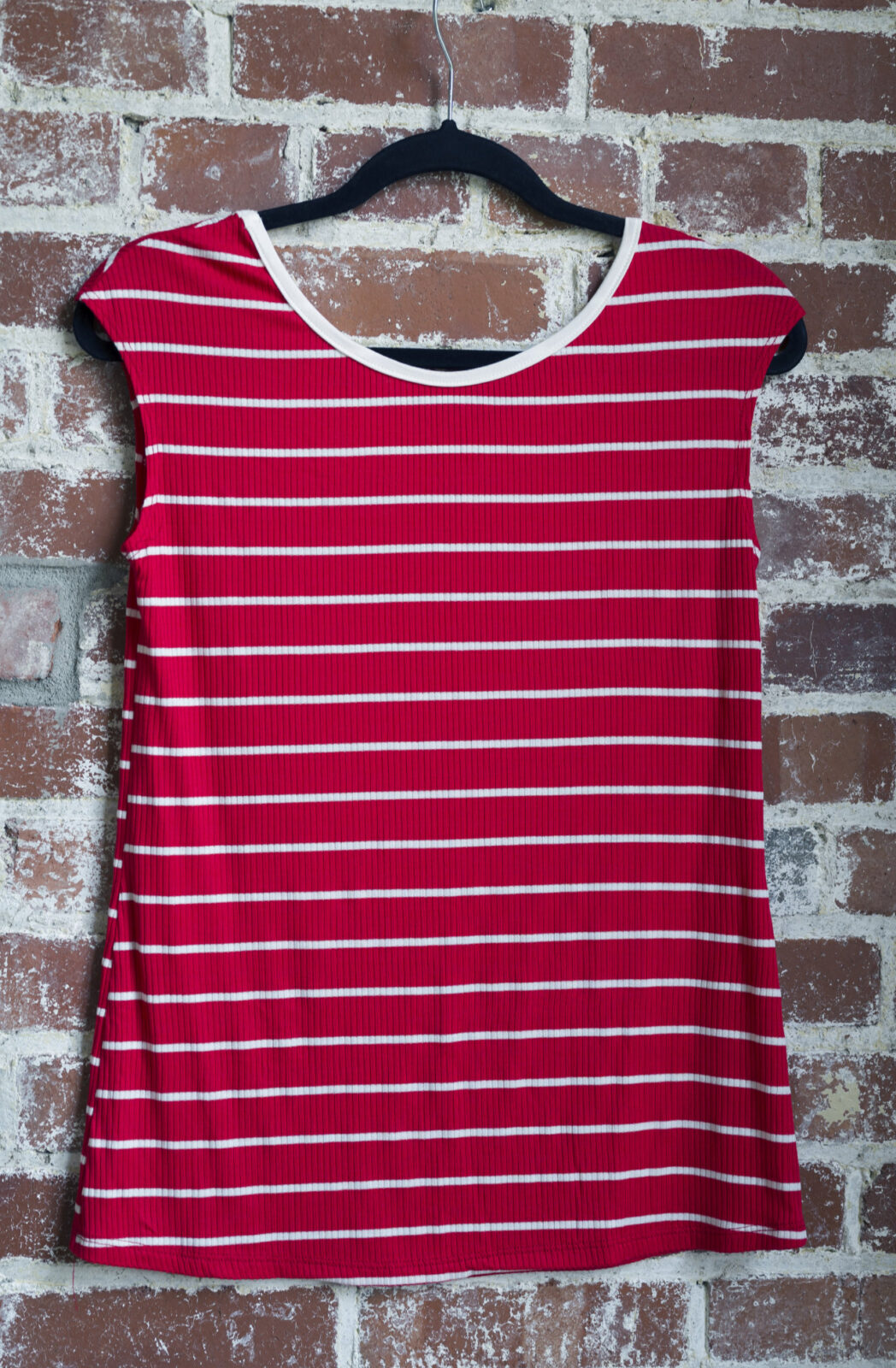 The Sol Top by Marie C in Red Stripe, with a scoop neck and cap sleeves, is shown hanging against a brick wall. 