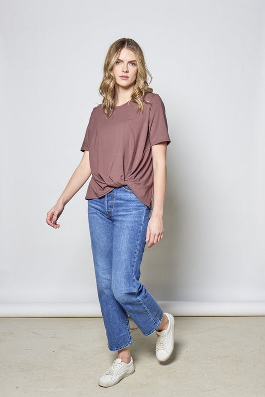 Woman wearing the Meriem Top by Tangente in Maroon and a pair of jeans, standing in front of a wall 