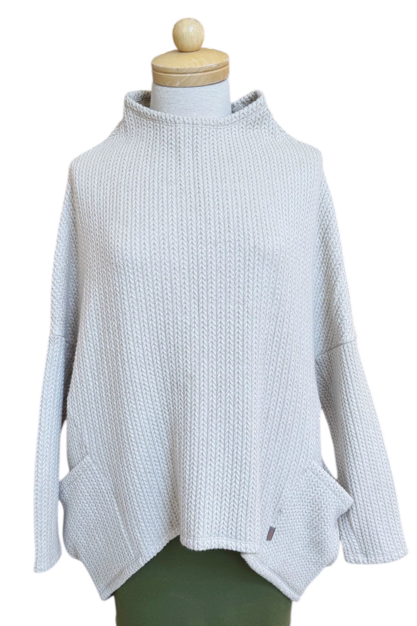 The Meeso Sweater by MOOVment in Oatmeal, a One Size oversized knit sweater with a wide mock turtleneck, long dropped sleeves and large side pockets, is shown on a mannequin in front of white background. 