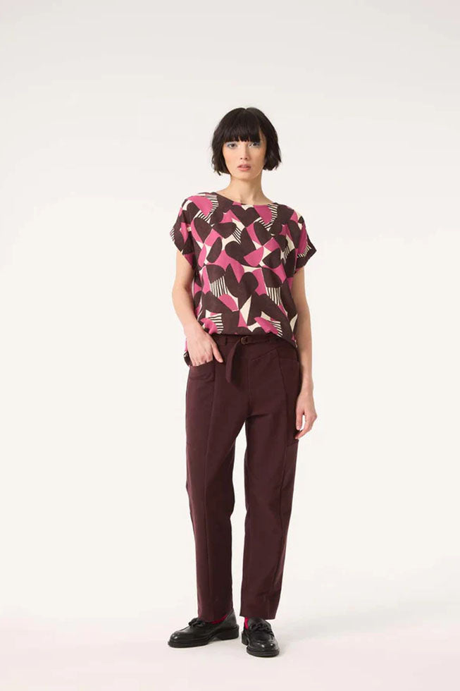 A woman wearing the Ombre Top by Cokluch in Berry Half Moon print with the Belief pants in Shiraz, standing in front of a white background. 