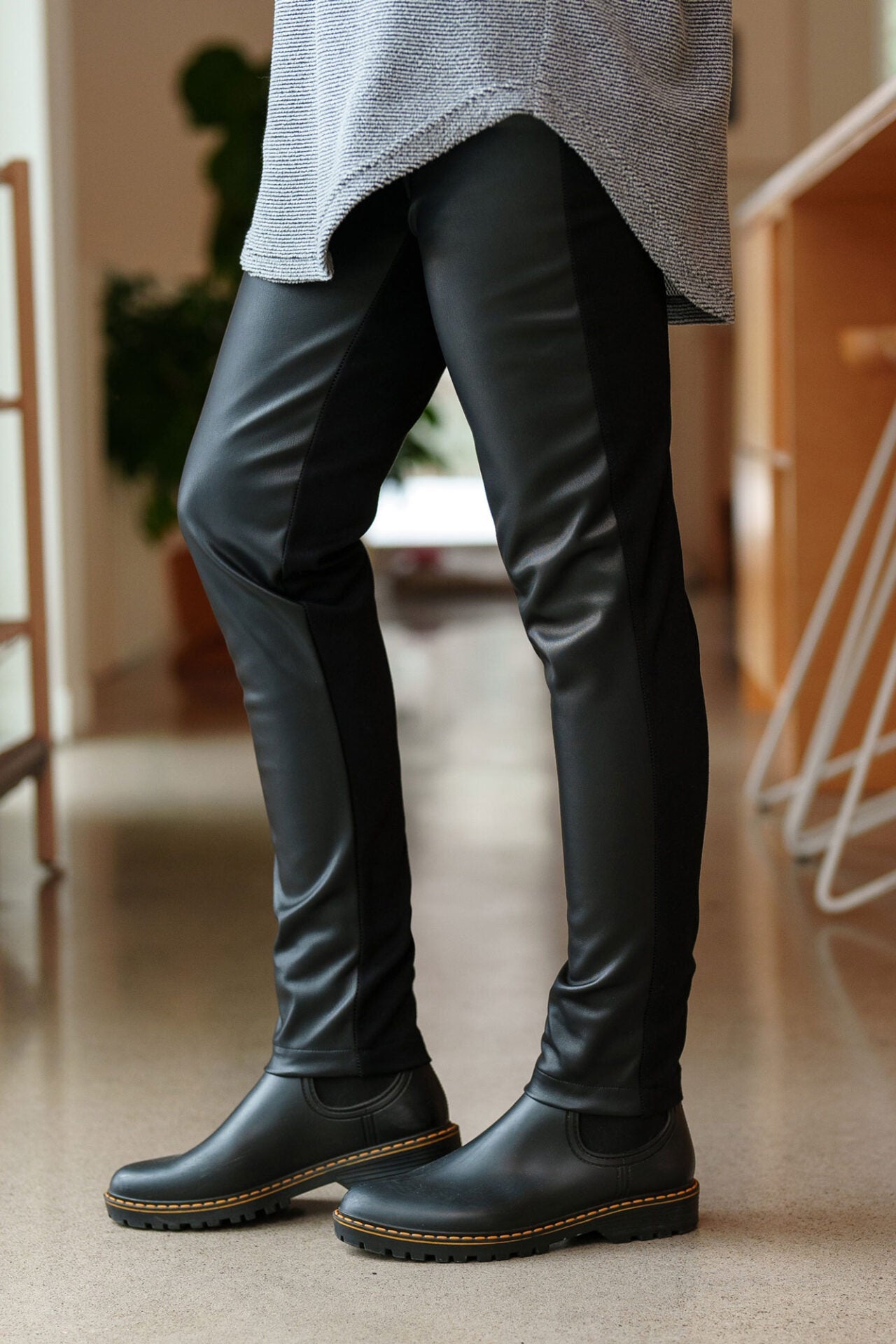 Close up side leg view of a woman wearing the Resinosa Pants by Rien ne se Perd in Black, slim fitting pants with faux leather at the front and plain fabric at the back, with a wide pull on waistband.