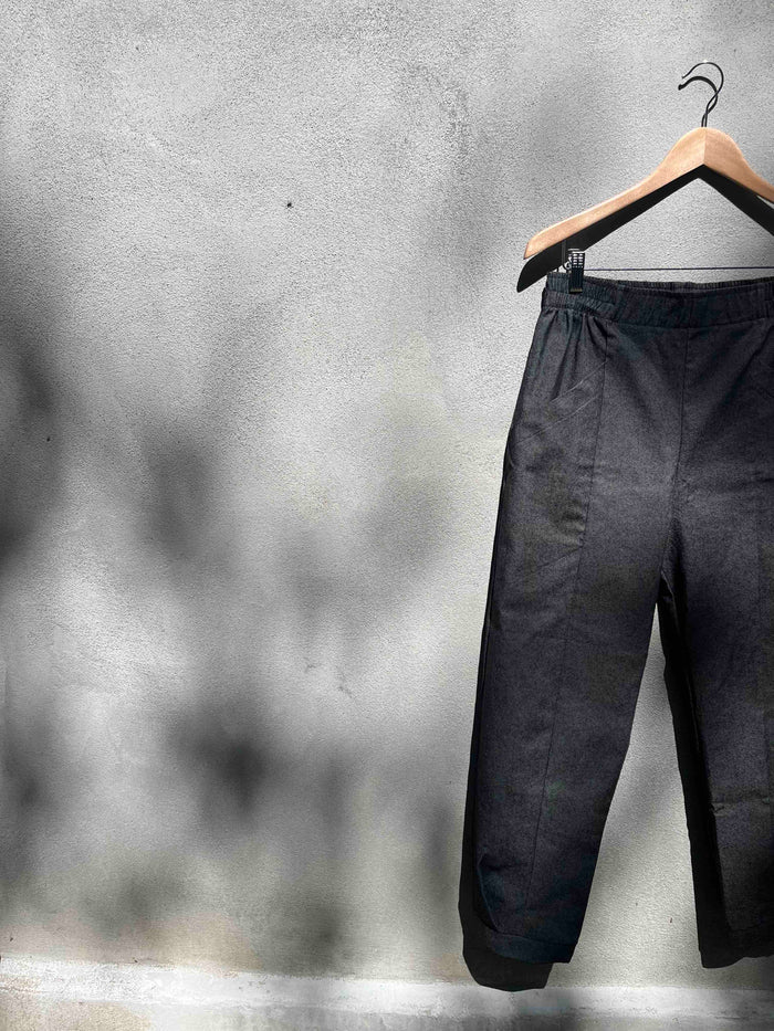 The Herbst Pant by Kazak in Black Denim, hanging against a grey wall 