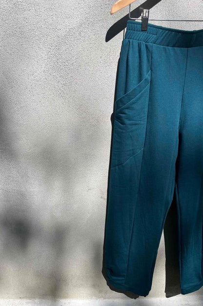 The Herbst Pant by Kazak in Teal Knit, hanging against a grey wall 