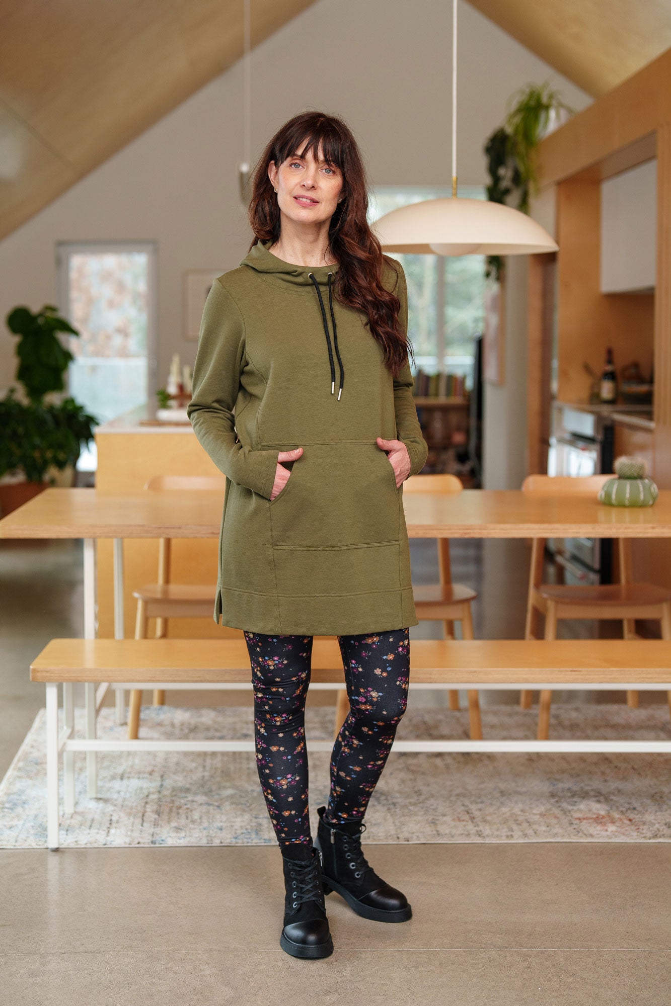 A woman wearing the Laracin Leggings by Rien ne se Perd in a small Floral print, with a green tunic. She is standing in a kitchen.