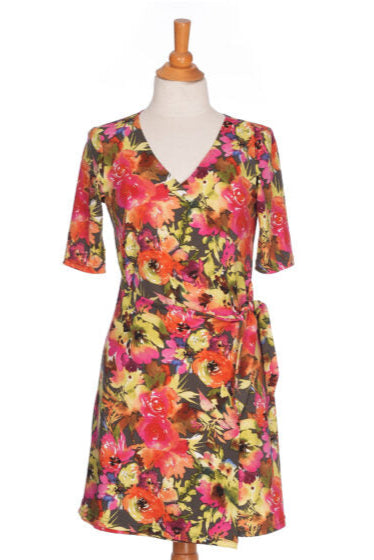 The Cha Cha Cha Dress by Rien ne se Perd, a faux-wrap dress in a floral pattern with a V-neck, tie at the waist, and knee-length A-line skirt, is shown on a mannequin in front of a white background. 