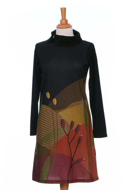 The Cornouiller Dress by Rien ne se Perd in Paysage print, featuring textured black fabric on the upper bodice and long sleeves and a landscape print on the body, with a cowl neck with a slit and coconut button detail, is shown on a mannequin in front of a white background.